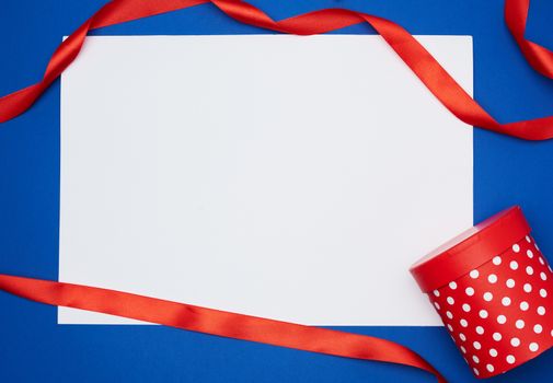 empty white sheet of paper and red silk twisted ribbon on a blue background, place for test, holiday backdrop