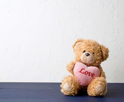 cute brown teddy bear holding a big pink heart and sits on a wooden background, holiday gift for Valentine's Day, copy space