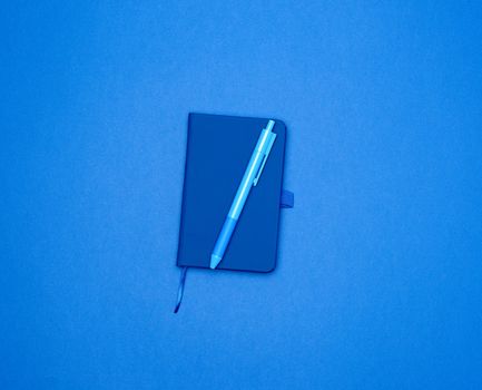 closed notebook and blue pen on a colored background, top view, flat lay