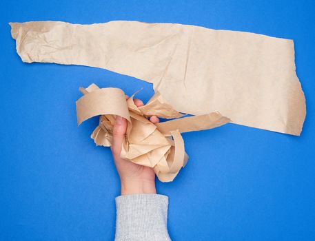 hand holds crumpled pieces of brown parchment paper on a blue background