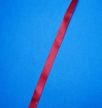 red silk thin ribbon on a blue background, close up