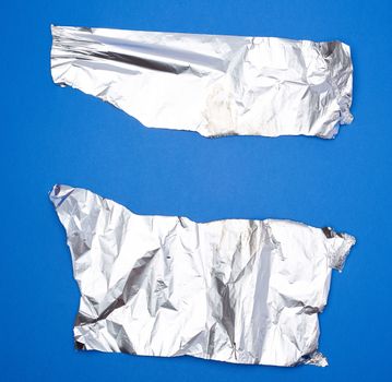 two torn silver pieces of baking foil on a blue background, creased parts with uneven edges