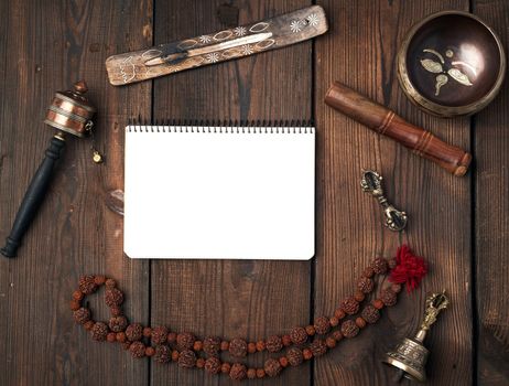 Copper singing bowl, prayer beads, prayer drum and other Tibetan religious objects for meditation and alternative medicine and open notebook on a brown wooden background