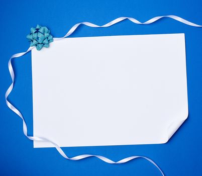 blank white sheet of paper with a curled corner and white ribbon on a blue background, copy space