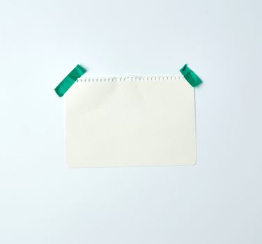 white crumpled sheet of paper torn from a spiral notebook and glued with green electrical tape on a white background, place for text