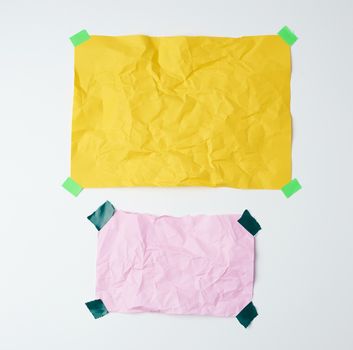 empty yellow and pink crumpled sheets of paper glued with green sticky pieces of paper on a white background, place for text