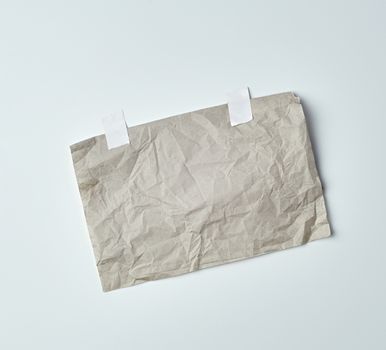gray crumpled sheet of paper glued with white adhesive tape on a white background, place for text