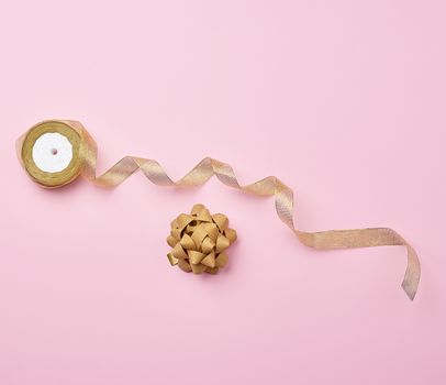 Shiny golden satin ribbon and bow on a pink background. Beautiful banner for celebration design. Anniversary, birthday