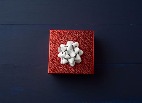 square red box tied with a golden ribbon, concept of congratulations and gifts, top view, blue wooden background