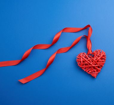 red wicker decorative heart hanging on silk ribbon, blue festive background for Valentine's day