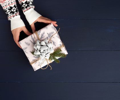 two female hands hold a paper closed box on a blue wooden background. Festive concept