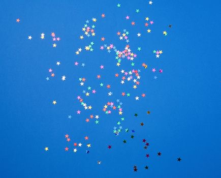 multicolored shiny confetti in the form of stars on a blue background, festive backdrop template. Bright festive decor