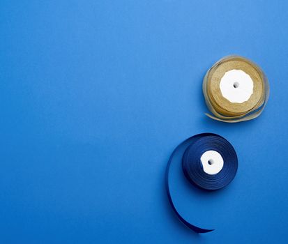 spools with blue and golden satin ribbon on a blue background, top view