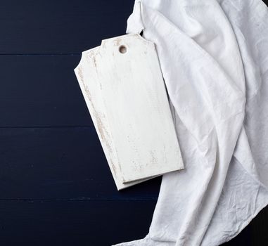 two rectangular white cutting kitchen boards on a blue wooden background, next to a white textile towel, top view. Copy space