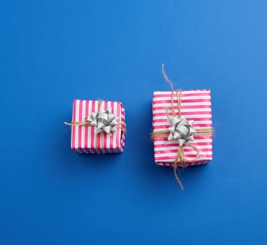 two gifts wrapped in pink striped paper on a blue background, top view, holiday backdrop 