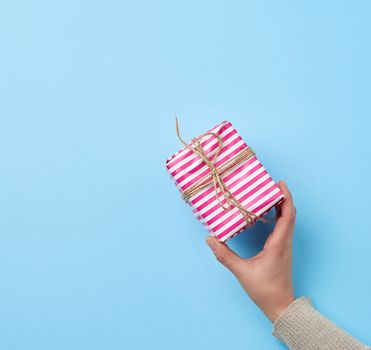 female hand holding a gift wrapped in a pink paper, blue background, top view