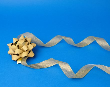 Shiny golden satin ribbon and bow on a blue background. Beautiful banner for celebration design. Anniversary, birthday