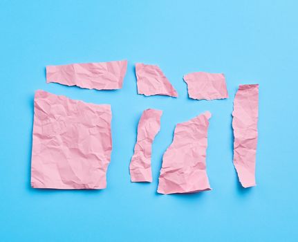 set of various cut pieces of pink crumpled paper on a blue background, close up