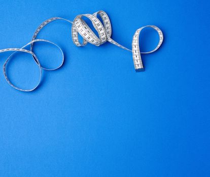 twisted white measuring tape on a blue background, copy space. Weight loss concept. Fitness background. 