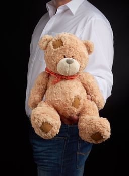 man in a white shirt holds a large teddy beige bear with patches, concept of a gift for Valentine's Day