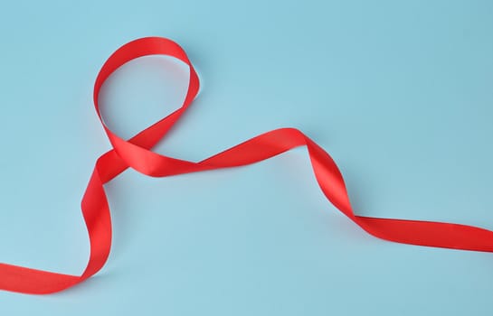 red silk thin ribbon twisted on a blue background, trendy classic color, close up