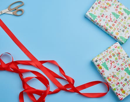gift wrapped in multi-colored paper and red ribbon on a blue background, festive backdrop, top view, copy space