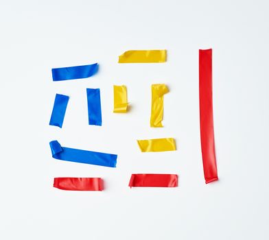 set of torn multicolored rubber pieces of electrical tape glued to a white background, close up