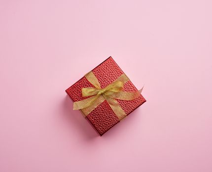 square red box tied with a golden ribbon, concept of congratulations and gifts, top view, pink background