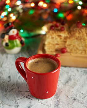 red ceramic cup with black coffee. near green branches of spruce and christmas toys.  Christmas season beverage.