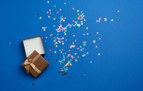 open square empty gift box on a blue background, near multi-colored sequins, top view, festive backdrop
