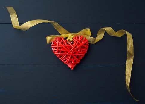 red wicker decorative heart hanging on golden silk ribbon, blue festive background for Valentine's day