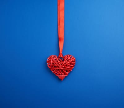 red wicker decorative heart hanging on silk ribbon, blue festive background for Valentine's day