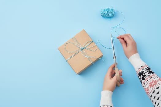 gift wrapped and tied with a brown rope, female hand with scissors cuts a brown rope, congratulation concept, copy space