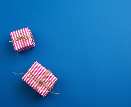 two gifts wrapped in pink striped paper on a blue background, top view, copy space