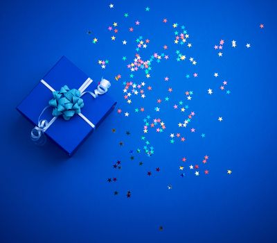 square blue shiny box with a bow and multicolored sparkles on a blue background, top view. Valentine gift
