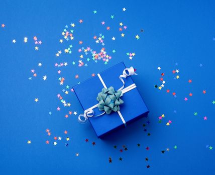 square blue  box with a bow and multicolored sparkles on a blue background, top view. Valentine gift