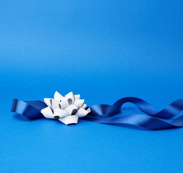 blue silk thin ribbon twisted and gray shiny bow on a blue background, trendy classic color, close up