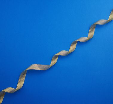 Shiny golden satin ribbon on a blue background. Beautiful banner for celebration design. Anniversary, birthday