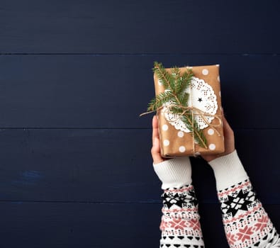 two female hands hold a paper closed box on a blue wooden background. Festive concept