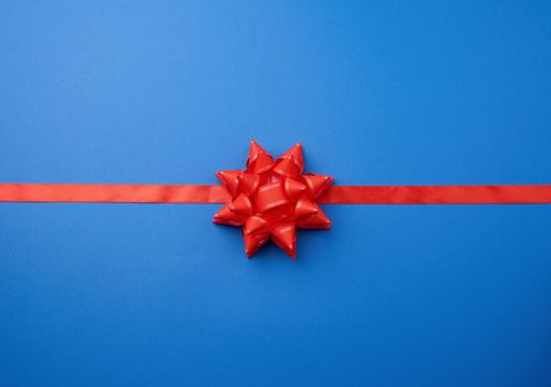 red silk ribbon and a large knotted bow on a blue background, imitation of gift packaging, festive creative backdrop