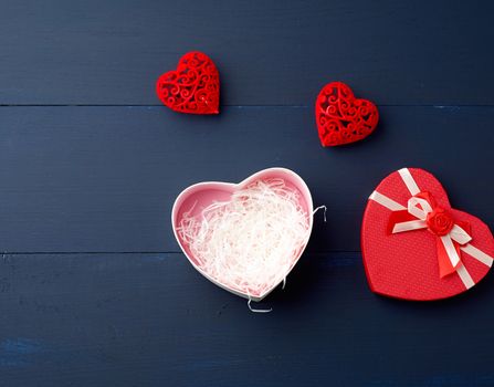 open red heart-shaped gift box with a bow on a blue wooden background, top view, festive backdrop