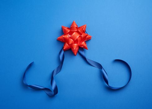 blue silk thin ribbon twisted and red shiny bow on a blue background, trendy classic color, close up