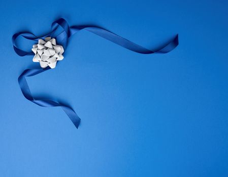 blue silk thin ribbon twisted and gray shiny bow on a blue background, trendy classic color, copy space
