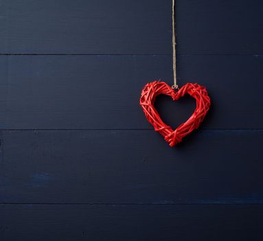 red wicker decorative heart hanging on brown rope, blue wooden festive background for Valentine's day