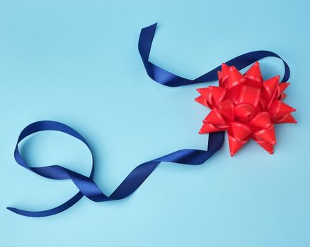 blue silk thin ribbon twisted and red shiny bow on a blue background, trendy classic color, close up