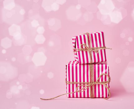 two boxes wrapped in christmas pink paper and tied with a brown rope on a pink background, blurred bokeh