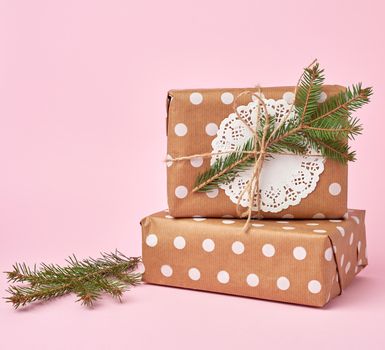 stack of kraft paper wrapped gifts, spruce branch on pink background. Christmas greeting concept