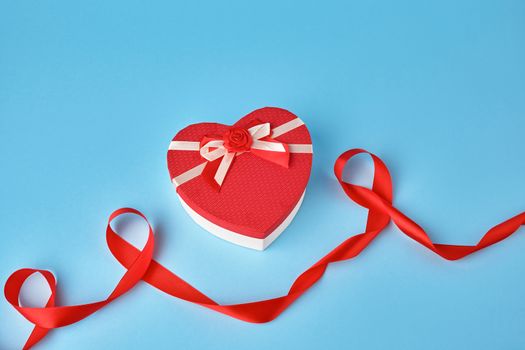closed red heart-shaped gift box with a bow on a blue background, top view, festive backdrop. Valentine gift