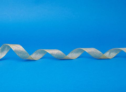 Shiny golden satin ribbon on a blue background. Beautiful banner for celebration design. Anniversary, birthday