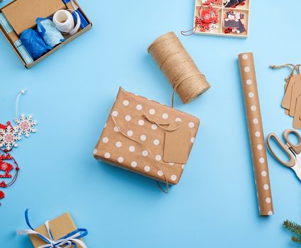 process of packing and wrapping boxes in festive brown paper, next to the luggage box decor on a blue background, top view. Christmas holiday concept